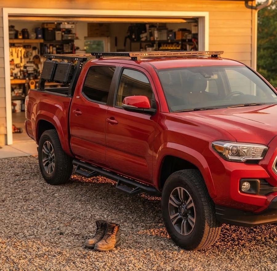 Overland truck bed rack loaded with a rooftop tent and recovery boards at a campsite